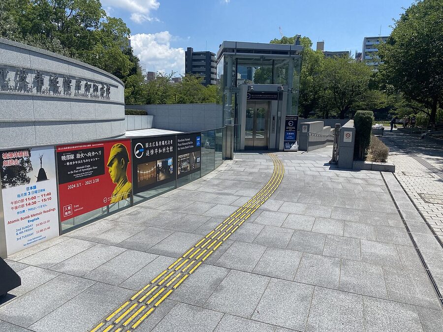 The entrance area of Hiroshima Peace Memorial Park with visitors walking along the tree-lined path