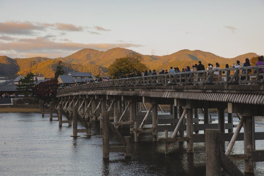 People crossing Togetsukyo Bridge in Arashiyama Kyoto at sunset with mountains behind