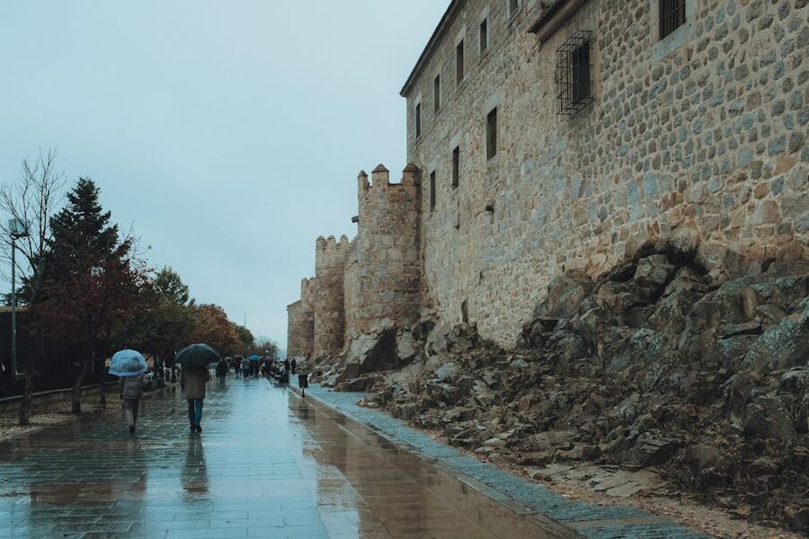 People walking along wet streets by the ancient walls of Avila Spain