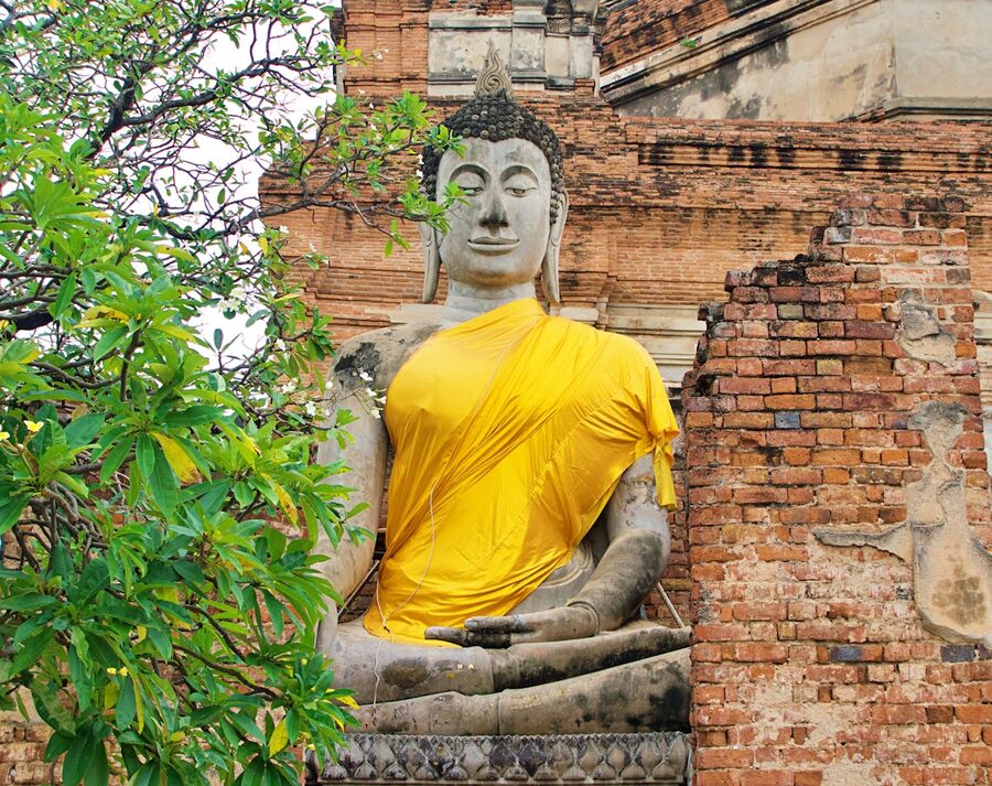 Peaceful Buddha statue draped in yellow cloth among ancient ruins at Wat Yai Chai Mongkhon Ayutthaya