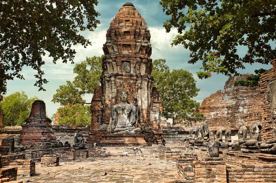 Stone Buddha statue surrounded by ancient brick temple ruins in Ayutthaya Thailand
