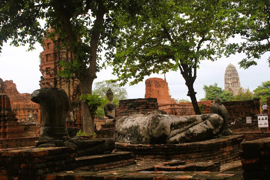 Row of weathered stone Buddha statues sitting among ancient ruins in Ayutthaya Historical Park