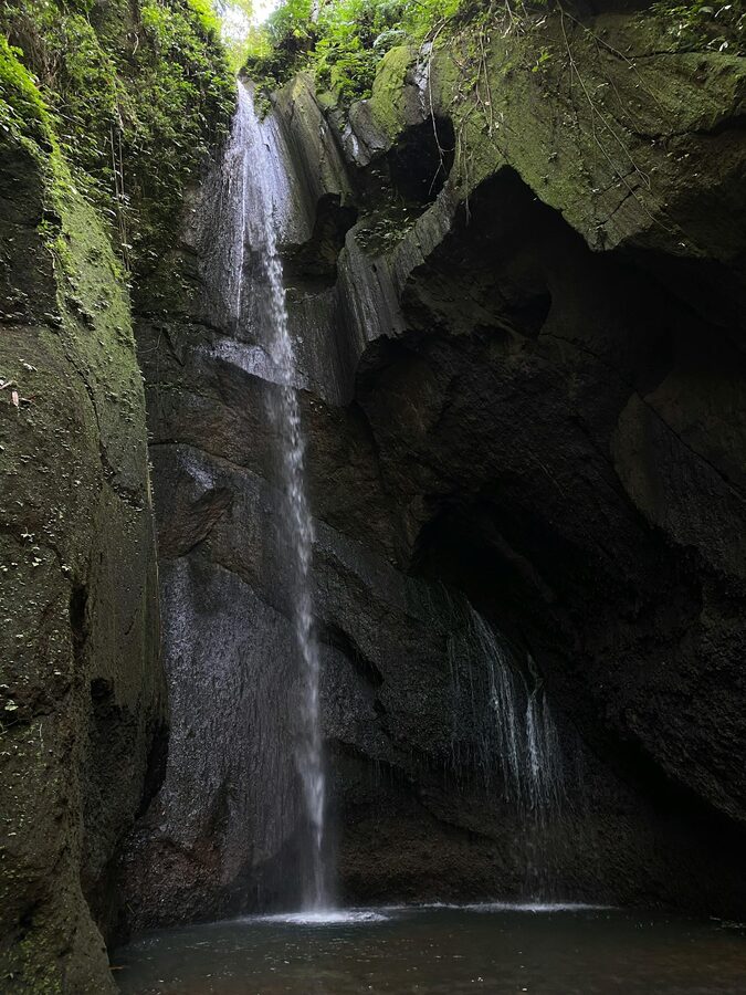 A traveler standing at the edge of a jungle plunge pool below a Bali waterfall