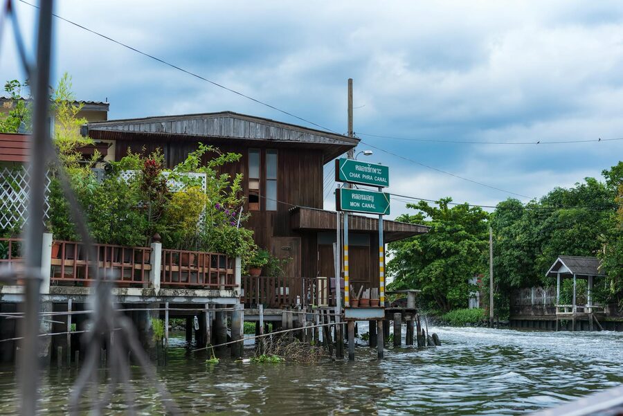 Rustic wooden house elevated on stilts beside a Bangkok canal under cloudy sky