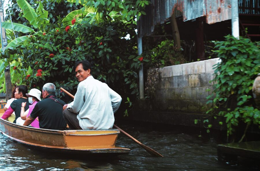 Passengers on a longtail boat cruising through a Bangkok canal surrounded by lush vegetation