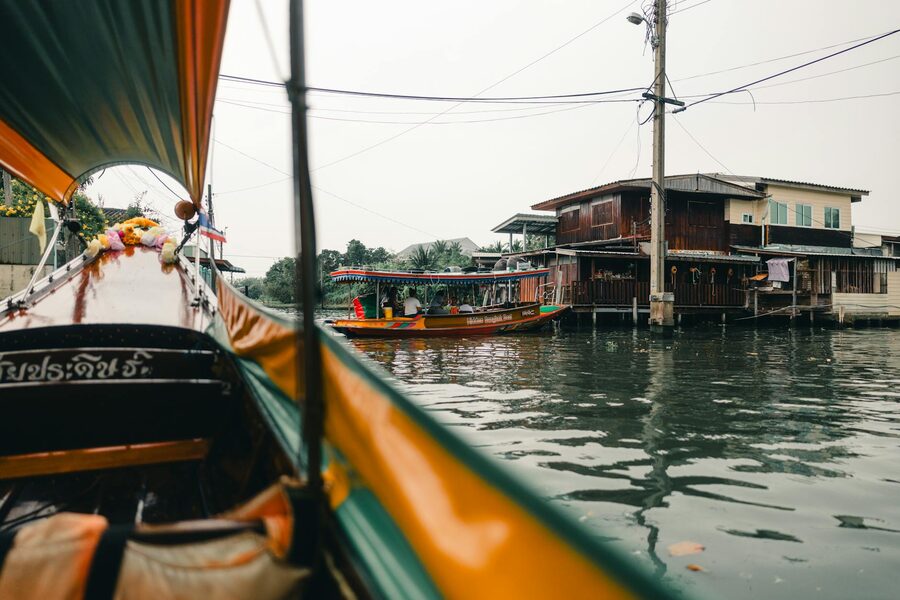 Boat cruising past traditional Thai houses along a Bangkok canal
