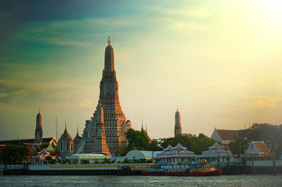Wat Arun temple silhouetted against an orange sunset sky from the Chao Phraya River