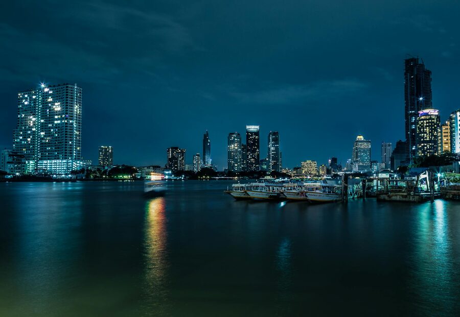 City skyline with boat lights reflecting in a river at night in Bangkok