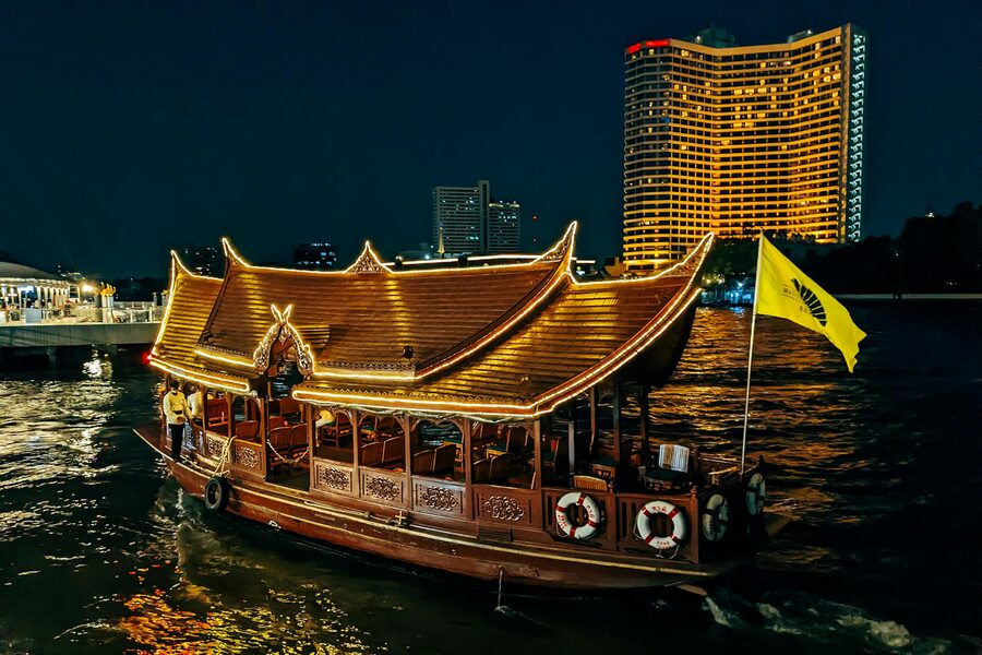 Ornate Thai wooden boat illuminated with lights on the Chao Phraya River at night