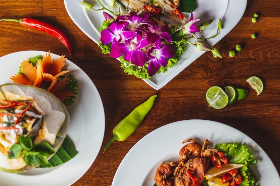 Multiple Thai dishes arranged on ceramic plates on a wooden table