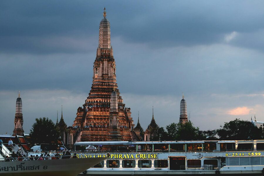 Cruise boat on the Chao Phraya River passing Wat Arun temple at sunset in Bangkok
