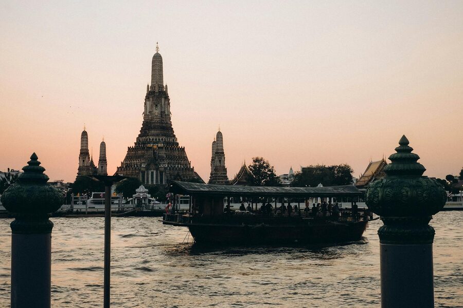 Scenic view of Wat Arun temple and a river ferry during sunset in Bangkok