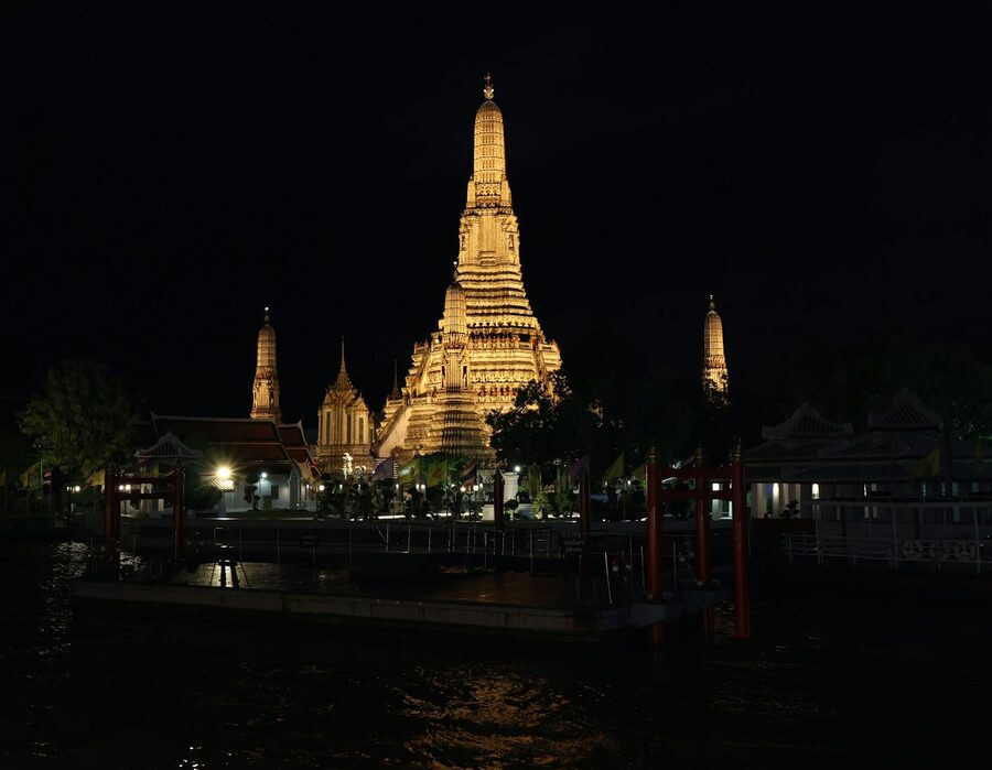 Wat Arun Temple glowing with lights at night seen from across the river in Bangkok