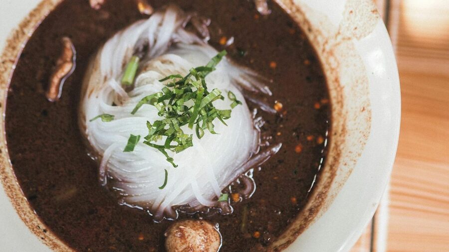 Bowl of Thai boat noodles with herbs in dark rich broth
