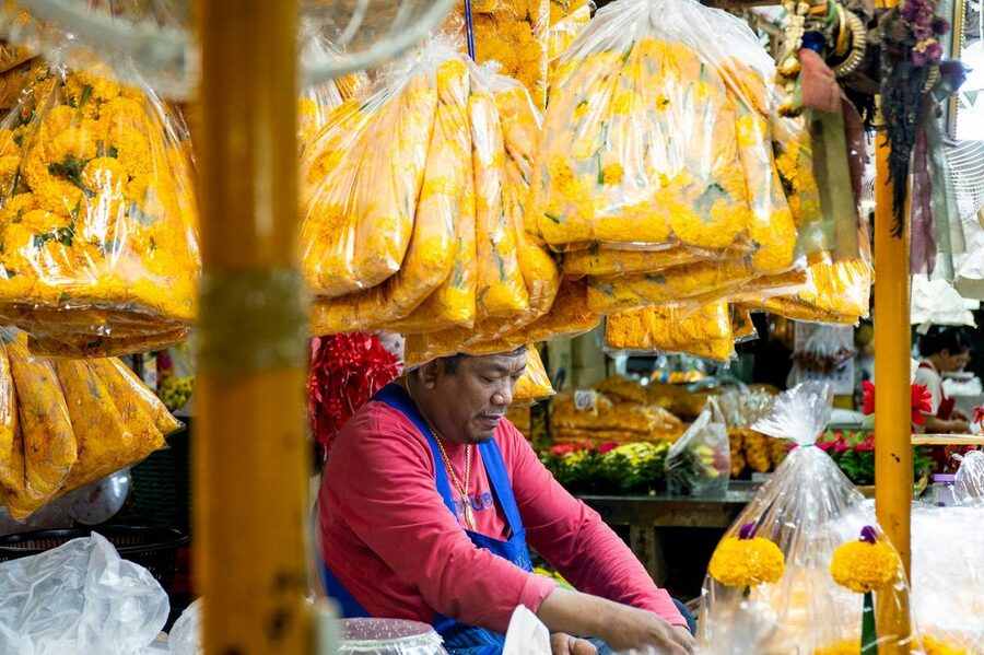 Vendor preparing colorful marigold flower garlands at Bangkok market