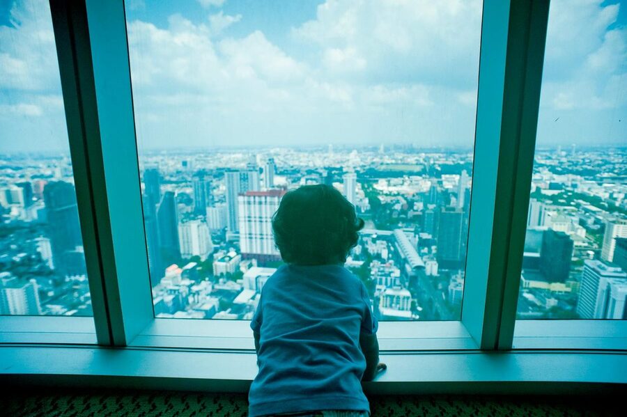 Child looking out over Bangkok skyline through observation window