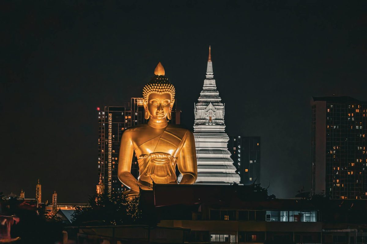 Large golden Buddha statue illuminated against Bangkok city skyline at night