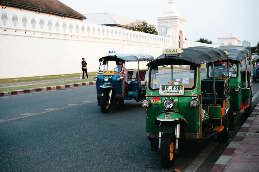Green and blue tuk-tuks parked by a wall on a Bangkok street