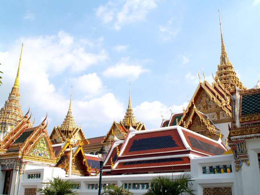 Golden spires and ornate architecture of the Grand Palace in Bangkok under blue sky