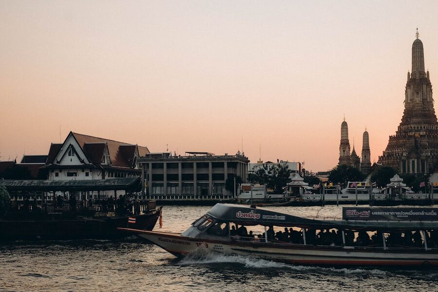 Scenic view of Wat Arun temple with a ferry boat on the Chao Phraya River at sunset in Bangkok