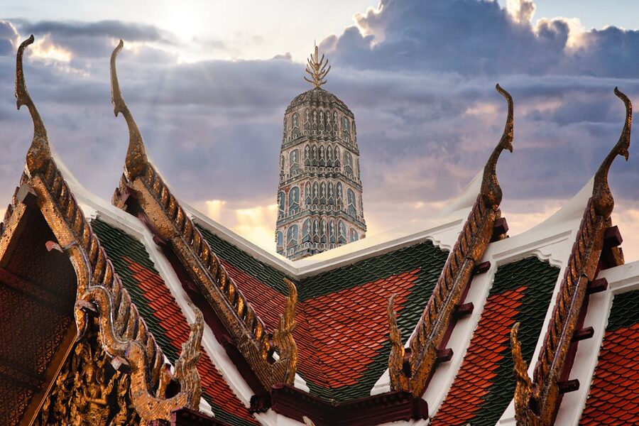 Ornate Thai temple rooftops with Wat Arun silhouetted against sunset sky in Bangkok