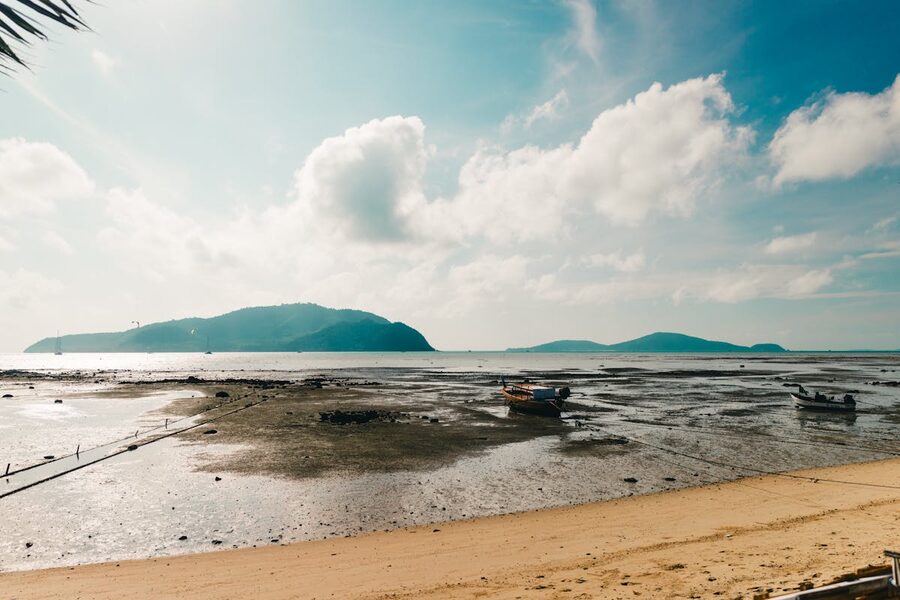 Scenic view of a tranquil Phuket beach with boats and mountains in the background