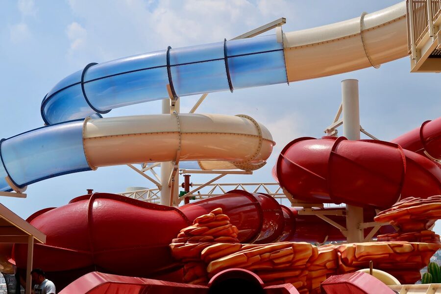 Red and blue water slides at an outdoor water park under clear blue sky