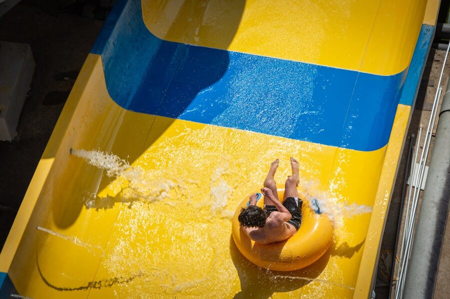 Person on inner tube going down a yellow and blue water slide in the sunshine