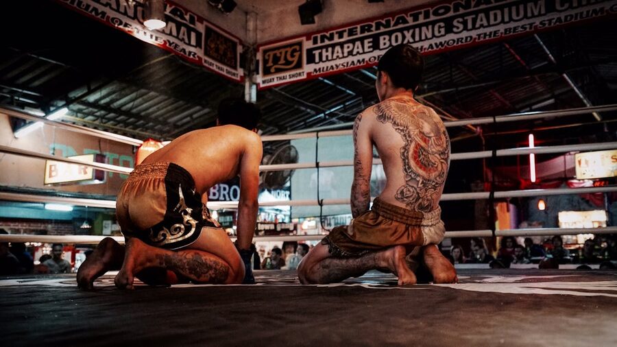 Two Muay Thai fighters kneeling in a boxing ring at Thapae Boxing Stadium
