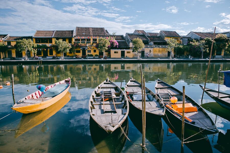 Traditional boats on a calm river reflecting yellow historic buildings in Hoi An Vietnam