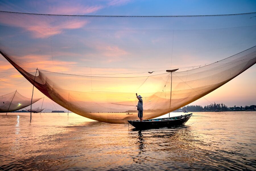 A fisherman casts a net at sunset on the waters of Hoi An Vietnam