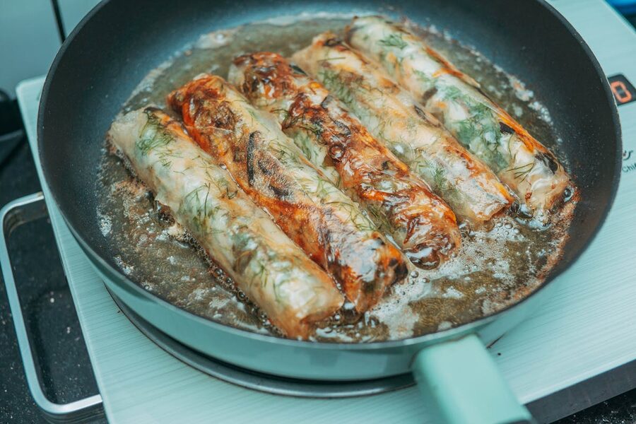 Crispy fried spring rolls sizzling in a pan over a stove