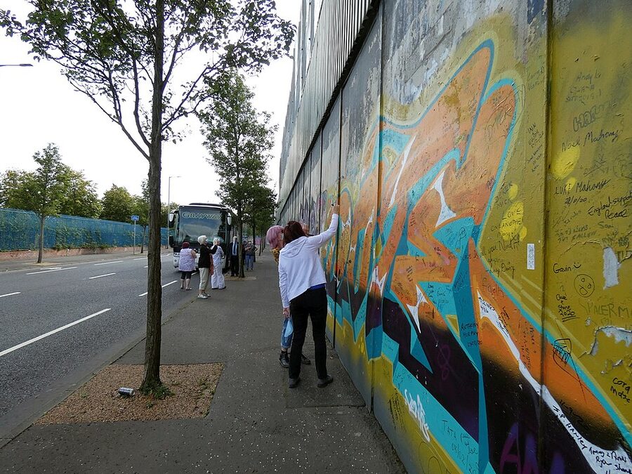 Visitor adding a message to the Belfast Peace Wall on Cupar Way