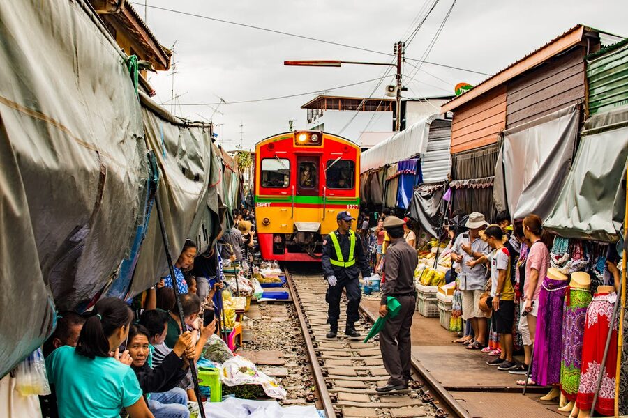 Train passing through Maeklong market with travellers and locals watching