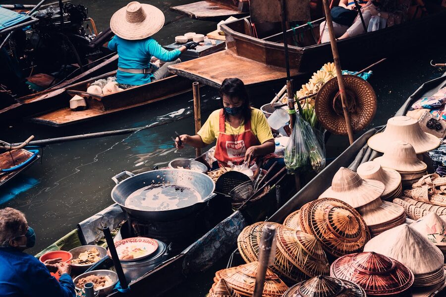 Vendor boats at a Thai floating market selling straw hats and food