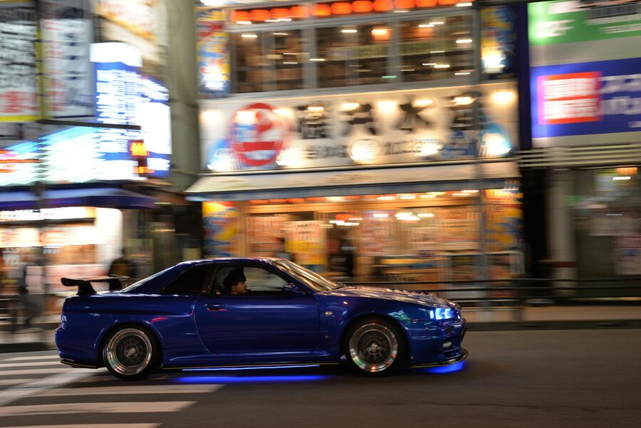 Blue sports car moving fast through neon-lit Tokyo streets