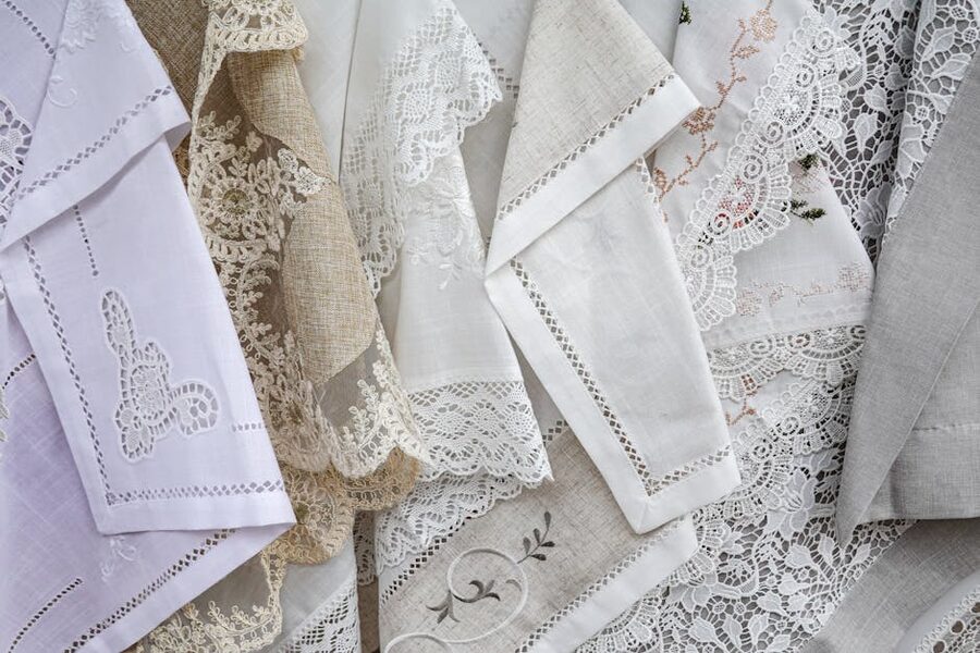 Burano lace and linen fabrics with intricate designs displayed at a market