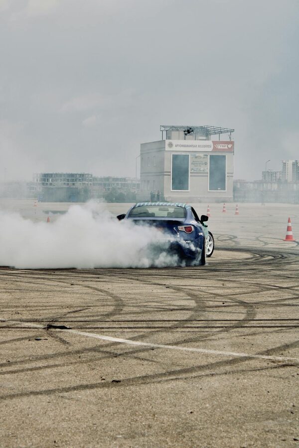 Blue car performing a drift on a race track surrounded by tire smoke