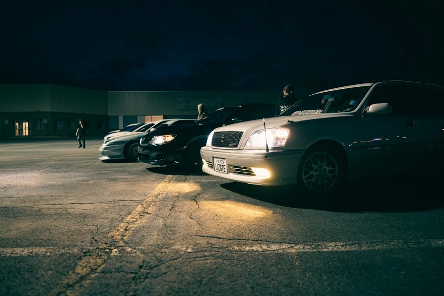 Row of cars under parking lot lights during a nighttime car meet