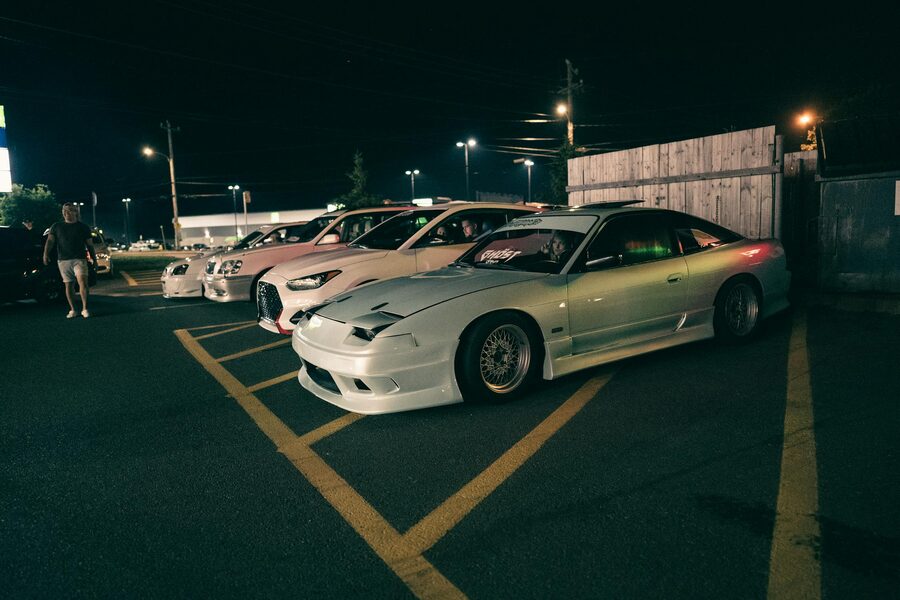 Sports cars lined up at a nighttime car meet in an urban parking lot
