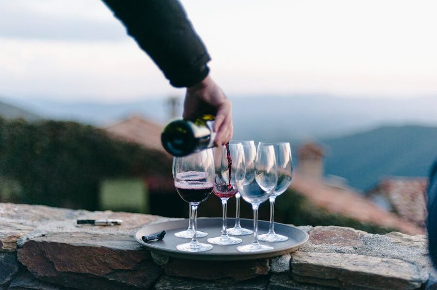 Hand pouring Chianti red wine into glasses outdoors with hills behind