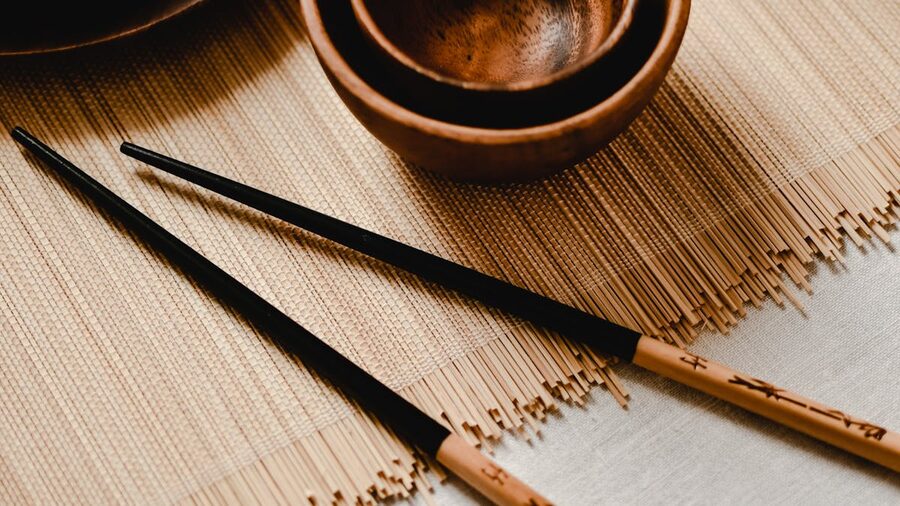 Close-up of wooden bowls and chopsticks resting on a bamboo mat in a minimalist arrangement