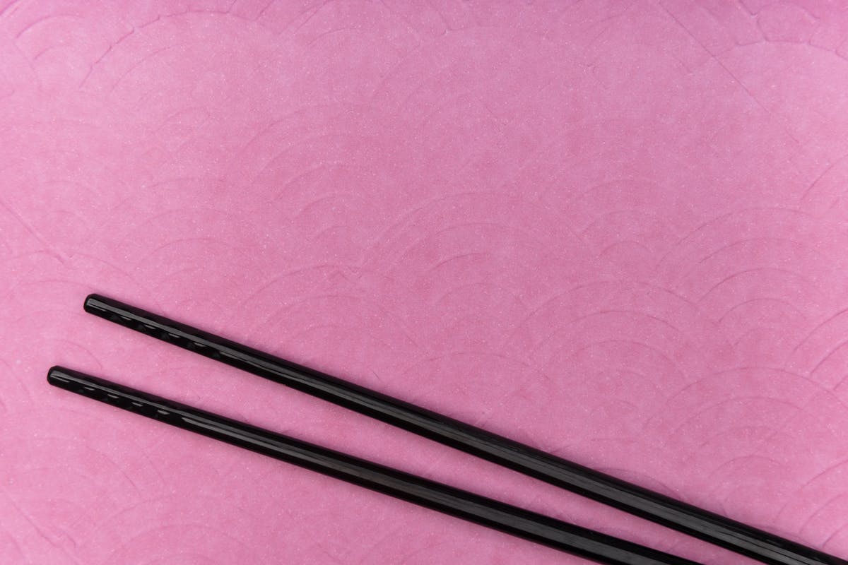 A pair of black lacquered chopsticks resting diagonally on a textured pink background