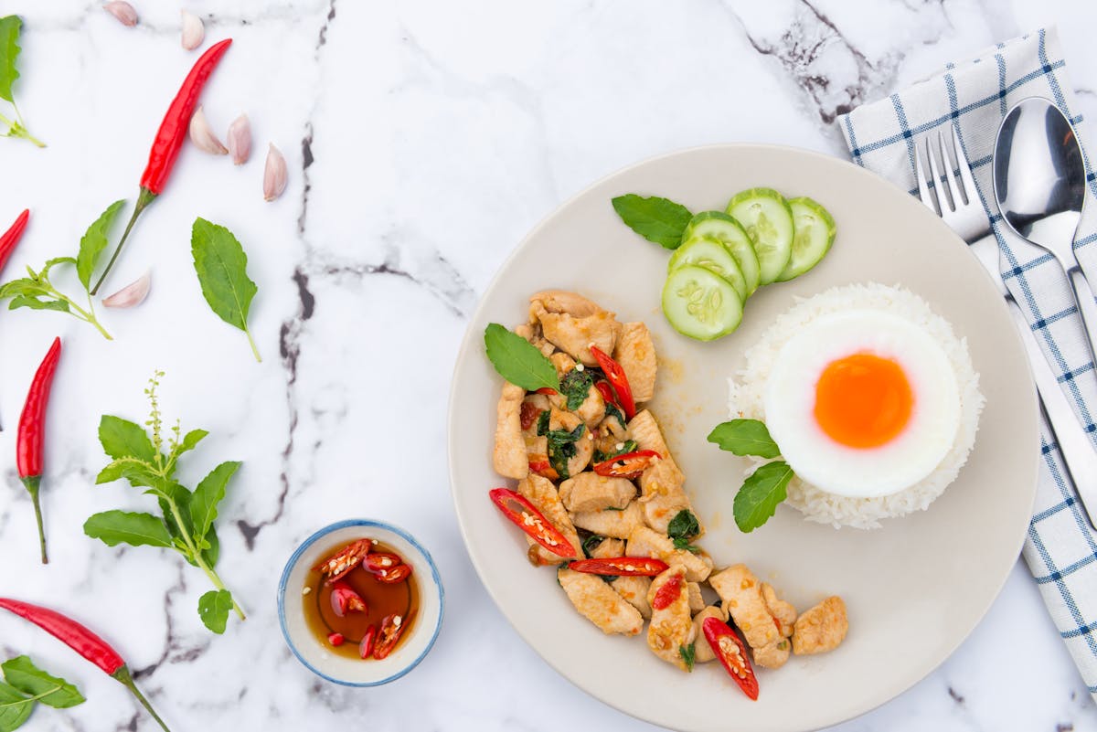 Thai meal with fried egg, basil chicken, rice, and cucumber