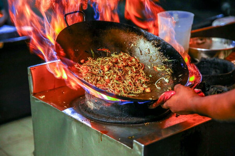 Chef cooking noodles in a flaming wok in a restaurant kitchen