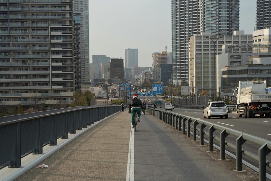Cyclist riding on a Tokyo highway surrounded by tall city buildings under a clear sky
