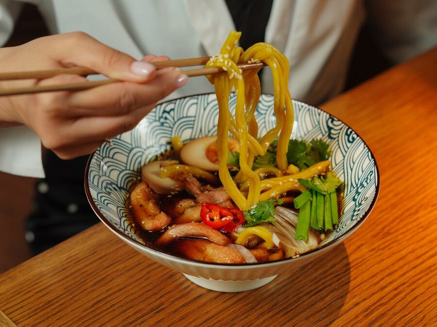 Close-up of a person using chopsticks to eat ramen from a bowl with colorful toppings