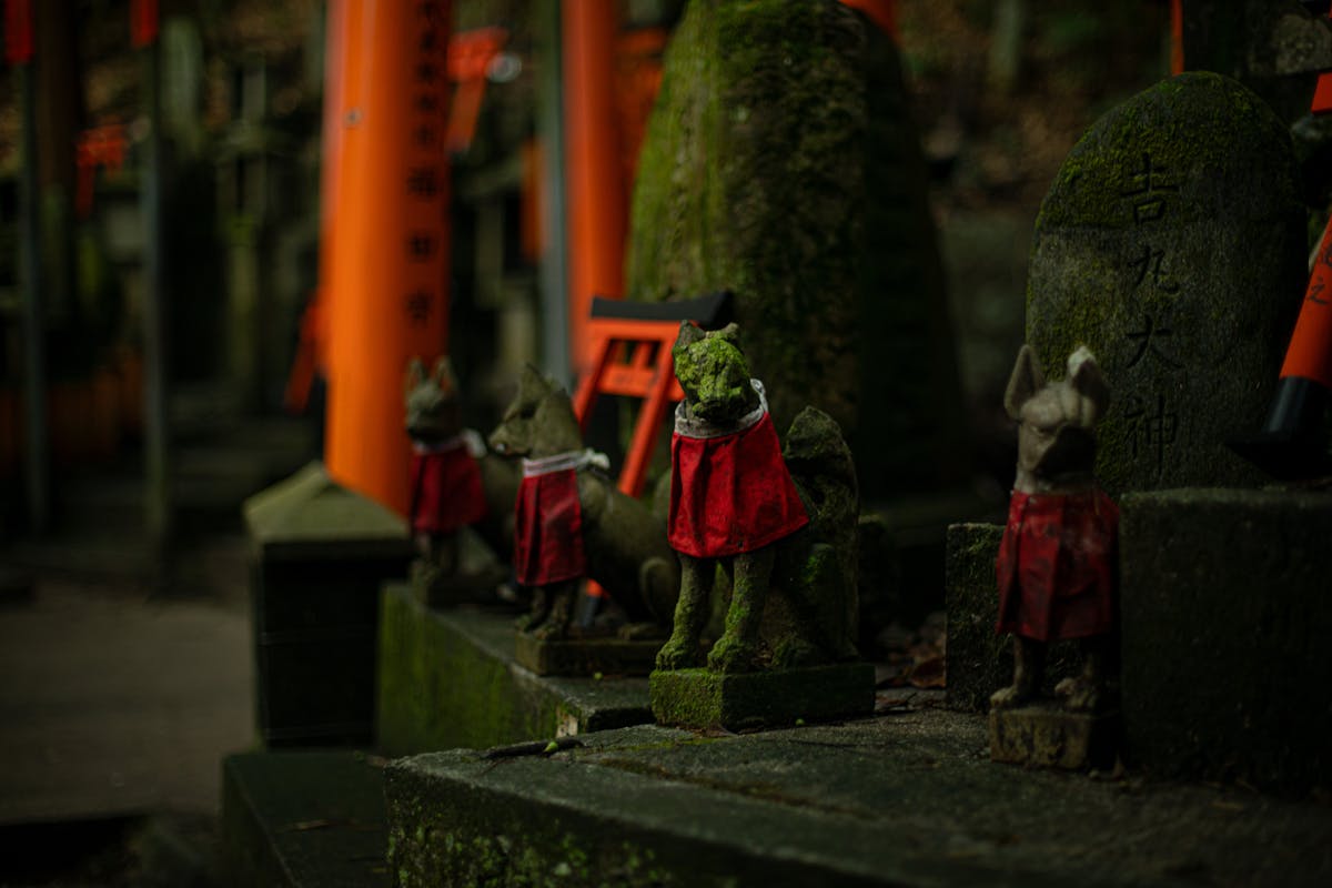 Moss-covered fox statues wearing red bibs at Fushimi Inari shrine