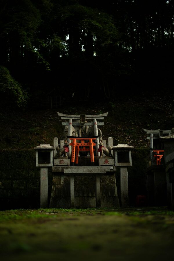 Stone fox statues and red torii gate in the forested section of Fushimi Inari Shrine
