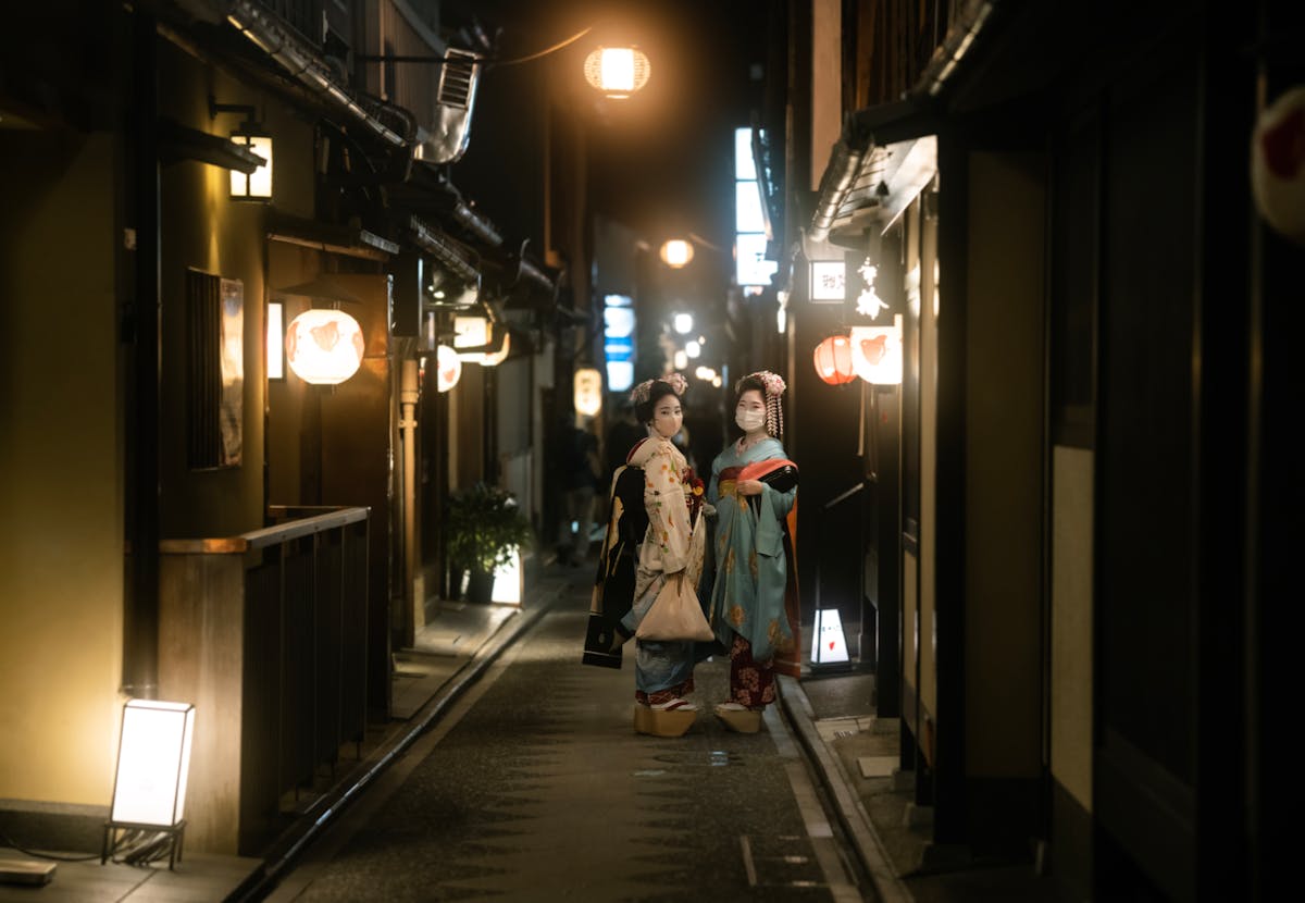 Two geishas in traditional attire strolling through the atmospheric streets of Kyoto